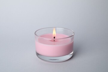 Fototapeta na wymiar Burning candle in glass holder on light grey background