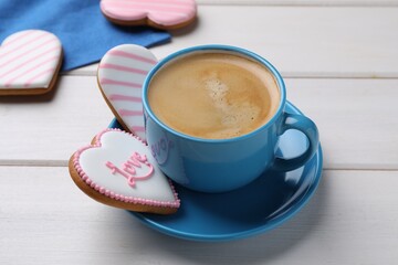 Delicious heart shaped cookies and cup of coffee on white wooden table, closeup