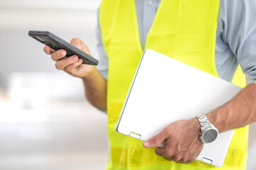 Male hand holding smartphone for check situatiob obout the work and the other hand holding laptop prepare to work at the construction site in the city.