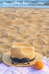 Hat with beautiful sunglasses and peach on sand near sea
