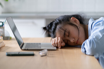 Tired Asian student girl lying on table in front of laptop, sleeping, taking break during online...