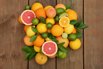 Naklejka na ściany i meble Different citrus fruits with green leaves on wooden table, flat lay