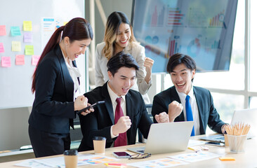 Millennial Asian young professional successful  businessman in formal suit laughing holding fists up celebrating with female and male businessman colleagues after winning job acheivement deal done