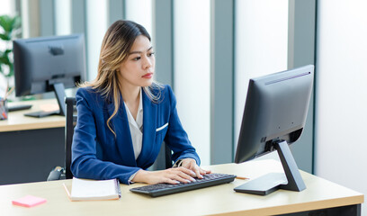 Millennial Asian young professional successful female businesswoman secretary employee in formal suit sitting working using pencil writing short note in notebook at company office workstation desk