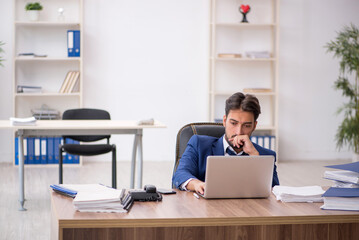 Fototapeta premium Young male employee unhappy with excessive work in the office