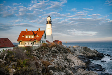 Fototapeta na wymiar An active lighthouse on a rocky shore of the Atlantic Ocean in the rays of the setting sun in the state of Maine in New England