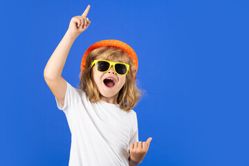Fashion portrait of kid in summer hat, t-shirt and sunglasses on blue studio isolated background....