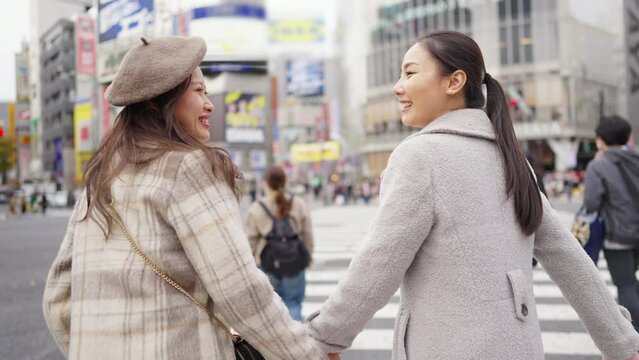 Asian woman friends crossing street crosswalk with crowd of people during shopping at Shibuya, Tokyo, Japan in autumn. Attractive girl  enjoy and fun outdoor lifestyle travel city on holiday vacation.