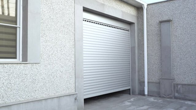 Opening roller shutter gate. Metal roller garage door as background. Automatic electric roll-up garage gate. Garage with rolling gates