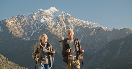 Old caucasian couple having a nordic walking hike in mountains, reaching the top of mountain and...