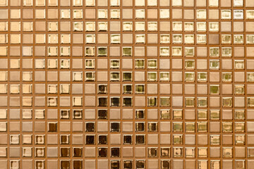 Close-up of golden-colored square glass tiles covering the bathroom wall texture as a background.