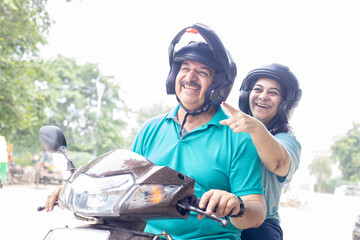 Happy senior indian couple wearing helmet riding motor scooter on road. Retirement life, Adventure and travel, Closeup