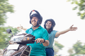 Happy senior indian couple wearing helmet riding motor scooter on road. Retirement life, Adventure and travel, Closeup © GAJENDRRA BHATI 