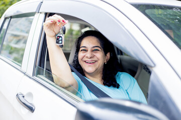 Happy indian mature woman sitting in car wearing seat belt show key with hand ready to drive. Just buy new vehicle