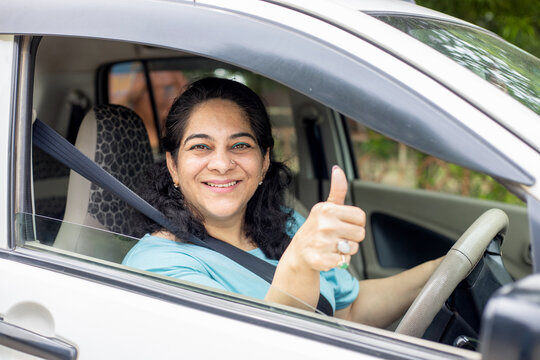 Happy indian mature woman sitting in car wearing seat belt do thumbs up with hand ready to drive. Safety and people concept.