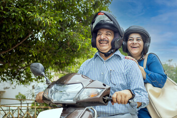 Happy mature indian couple wearing helmet riding motor scooter on road. Retirement life, Adventure and travel, Closeup