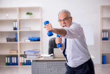 Naklejka na ściany i meble Old male employee doing sport exercises at workplace