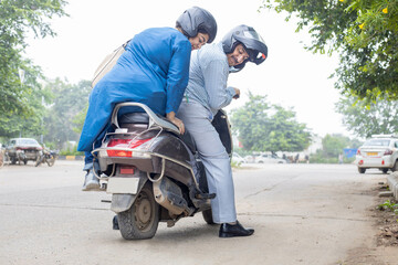 Mature indian couple sitting on motor scooter with flat tire.