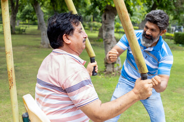 Indian mature senior men exercises on the public park gym equipment outdoor.