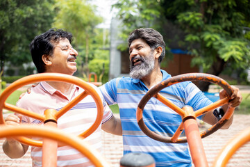 Indian mature senior men exercises on the public park gym equipment outdoor.