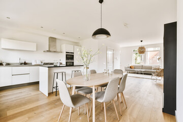 a kitchen, dining room and living area in an apartment with white walls and wood flooring the table is surrounded by grey chairs