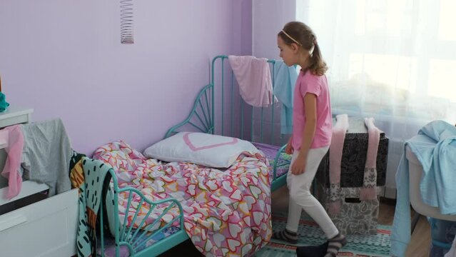 Little girl making her bed while cleaning her messy room. Concept of household chores and housework