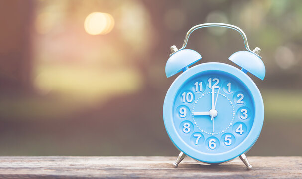 Light blue alarm clock on nature background with bokeh and space for text, time concept.