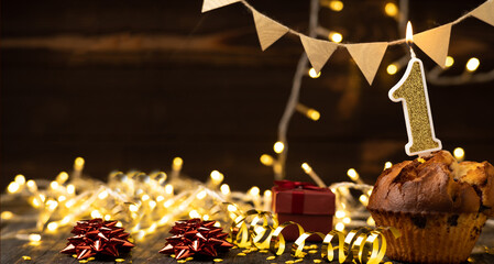 Number 1 gold burning candle in a cupcake against celebration wooden background with lights. Birthday cupcake. Copy space