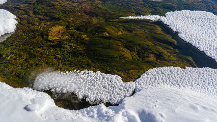 Thawed stream in early spring. Close-up. Algae on the bottom are visible through the clear water. Fluffy frost on the surface. Altai