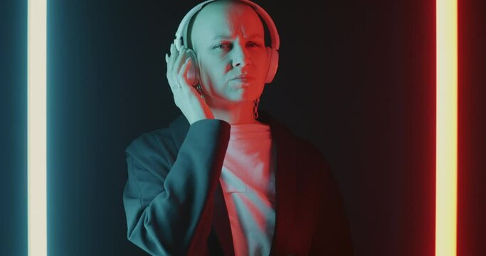 Slow motion of young woman wearing headphones dancing having fun on beautiful black background with neon lamps. Entertainment and devices concept.