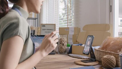 SME owner go green net zero retail store live stream talk on phone showing eco care plastic free packaging box. Asia people young woman record video on tiktok IG reel instagram shop happy side hustle.