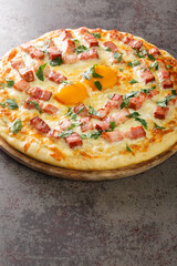 Hot pizza carbonara with bacon, egg, cheese and herbs close-up on a wooden board on the table. Vertical