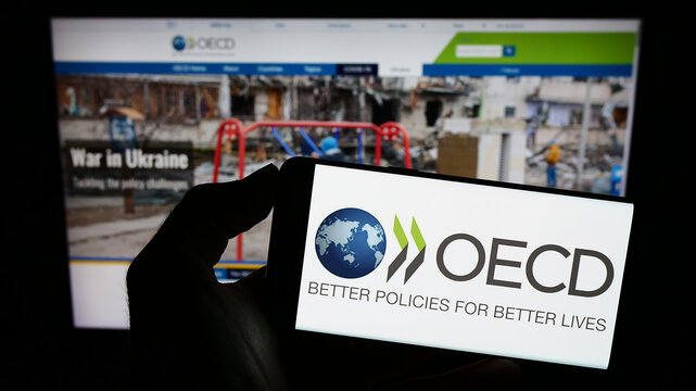 Stuttgart, Germany - 12-23-2022: Person holding cellphone with logo of intergovernmental organisation OECD on screen in front of webpage. Focus on phone display.
