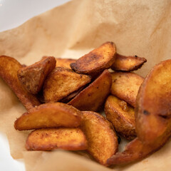 Fried potato wedges on baking paper. French fries. Oven baked. Vegetable garnish. Vegetarian dish. Rustic potatoes. Copy space. Close-up. Soft focus.