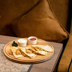 Pita with stuffing and sauces on wooden board. Asian cuisine. Sliced pita bread with red and white sauce. Dish on table against background of sofa. Quick snack. Soft focus, side view. Copy space.