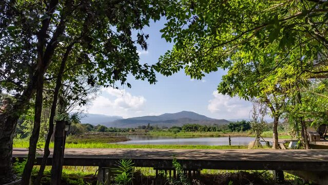 Time lapse of distant mountains in Hod, Chiang Mai, Thailand with trees, rice paddy field and pond in foreground
