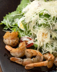 Salad with vegetables, lettuce, shrimp eggs and cheese served on a black plate. Seafood food. Dark background. Top view. 