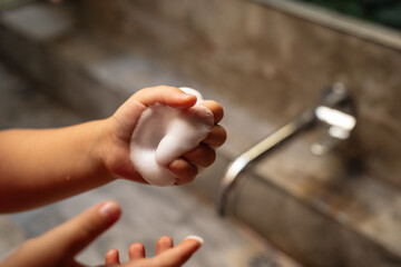 The habit of washing hands. Foam for washing hands with antibacterial properties in the hands of a child against the background of a stone washstand.