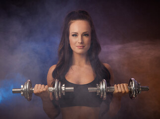 Beautiful young woman works out with dumbbells in fitness gym