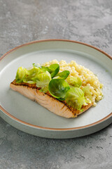 Close up view of grilled salmon served with Brussel sprouts and Ptitim over grey background