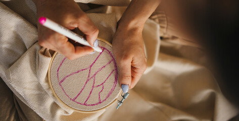 Close-up view of a woman's hands making a sketch of the design she wants to embroider on the white...