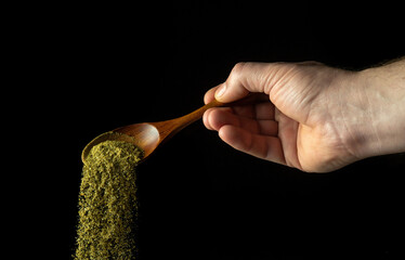 Mixture of dry chopped herbs is poured from a wooden spoon to add to a medicinal drink or tea. Free...