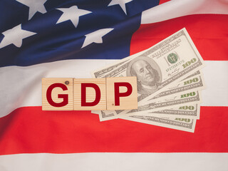 GDP or gross domestic with wooden cubes on US dollar banknotes over the American flag background