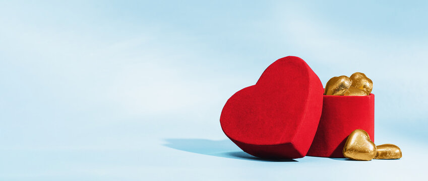 Golden chocolate hearts in and near red velvet heart box on blue background. St Valentines or Mothers day greeting card. Thank you sweets. Side view banner