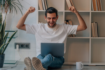 young man at home elated with laptop celebrating