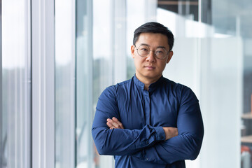 Portrait of asian businessman inside modern office, boss in glasses serious looking at camera, man...
