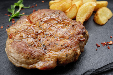 Grilled steak with fried potatoes, on a black plate