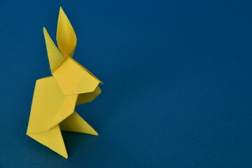 Yellow origami paper rabbit on blue background.