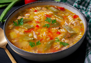 Minestrone, italian vegetable soup with pasta on black table.