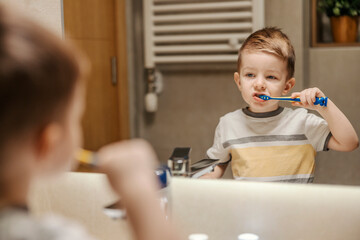 A little boy is brushing his teeth in bathroom in the morning.